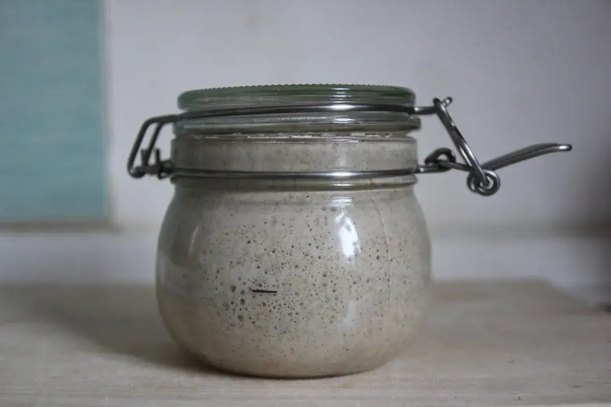 Un tarro de cristal con una masa madre casera burbujeante y activa, lista para hornear pan.