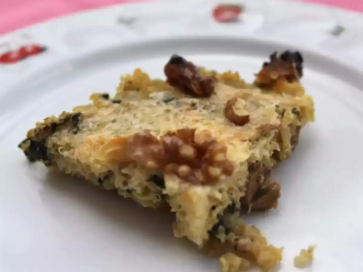Rebanada de pizza de quinoa con nueces y trozos oscuros, servida en un plato blanco.