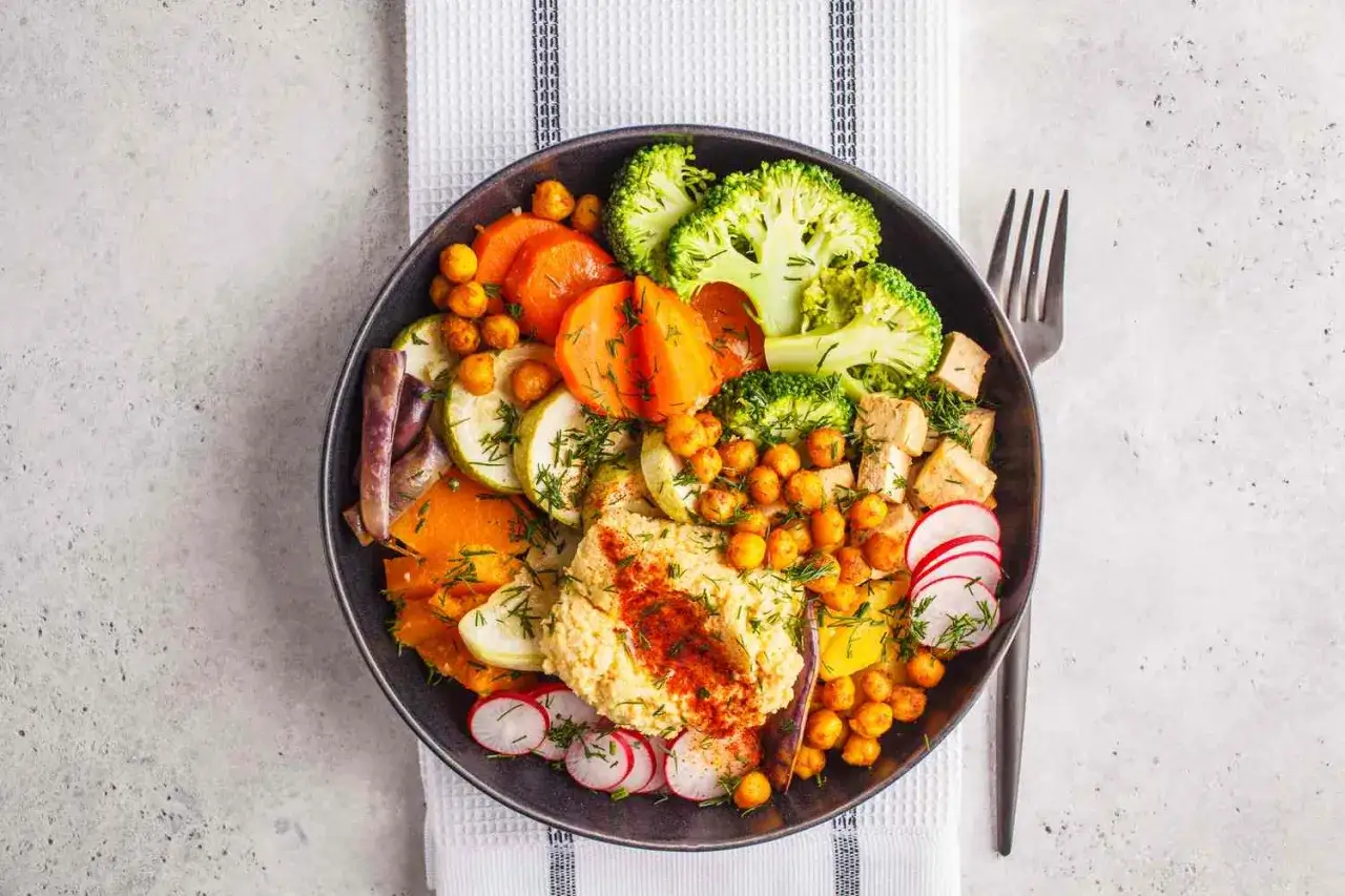 Un plato vibrante con hummus, brócoli, zanahoria, calabacín, garbanzos y rábano, perfecto para una dieta macrobiótica equilibrada.