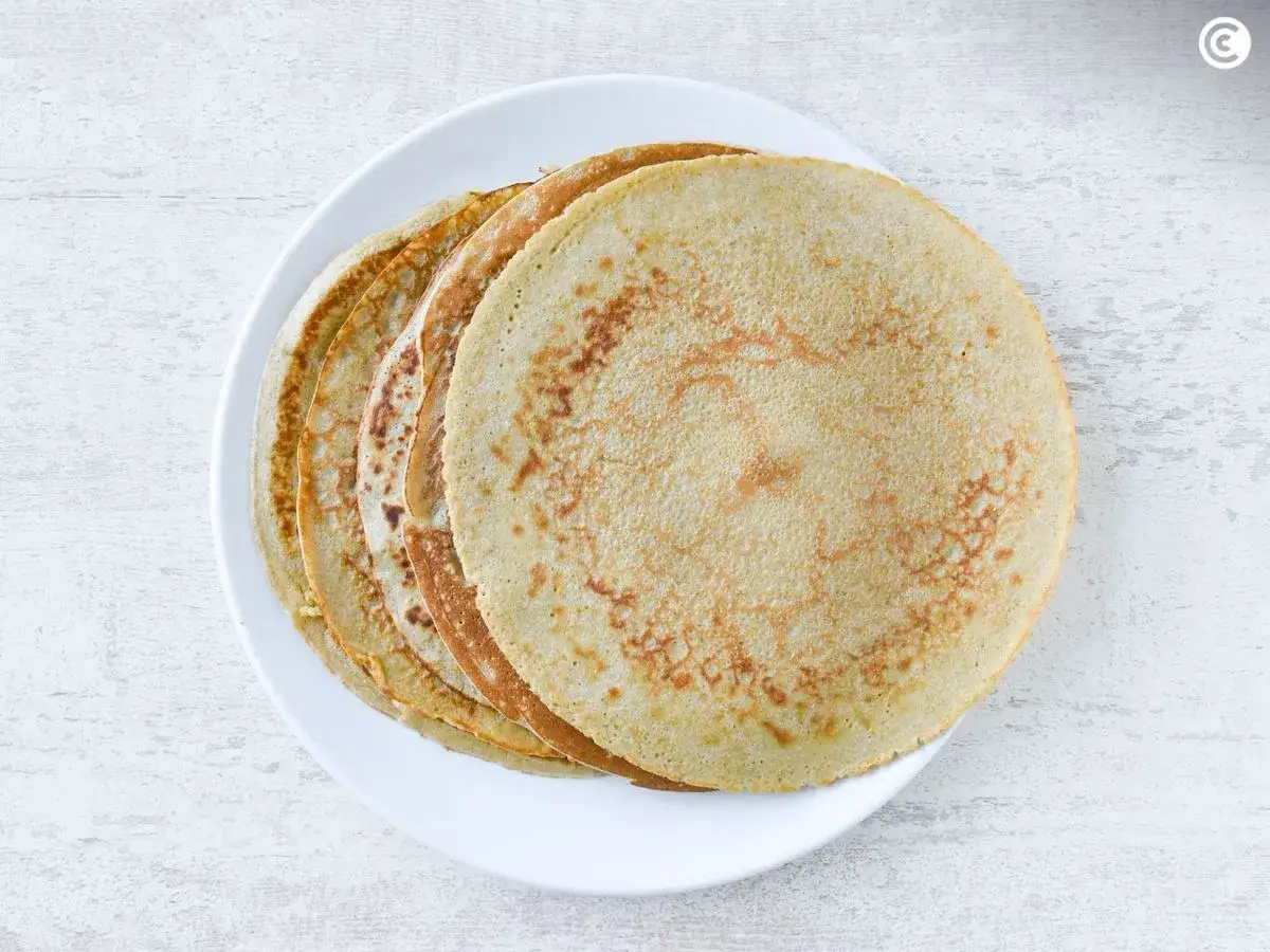 Una pila de crepes de avena dorados y finos sobre un plato blanco, listos para disfrutar.