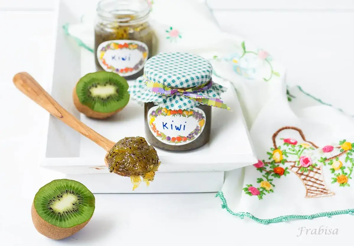 Cuchara con mermelada de kiwi casera, junto a kiwis frescos y frascos decorados.