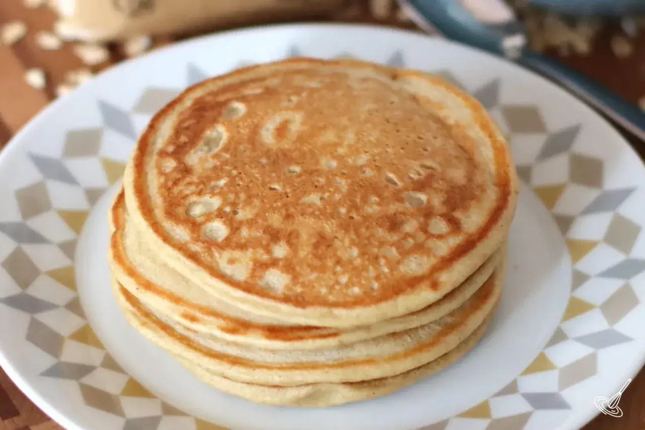Una pila de deliciosos pancakes de avena dorados, servidos en un plato blanco con dise&ntilde;o geom&eacute;trico.