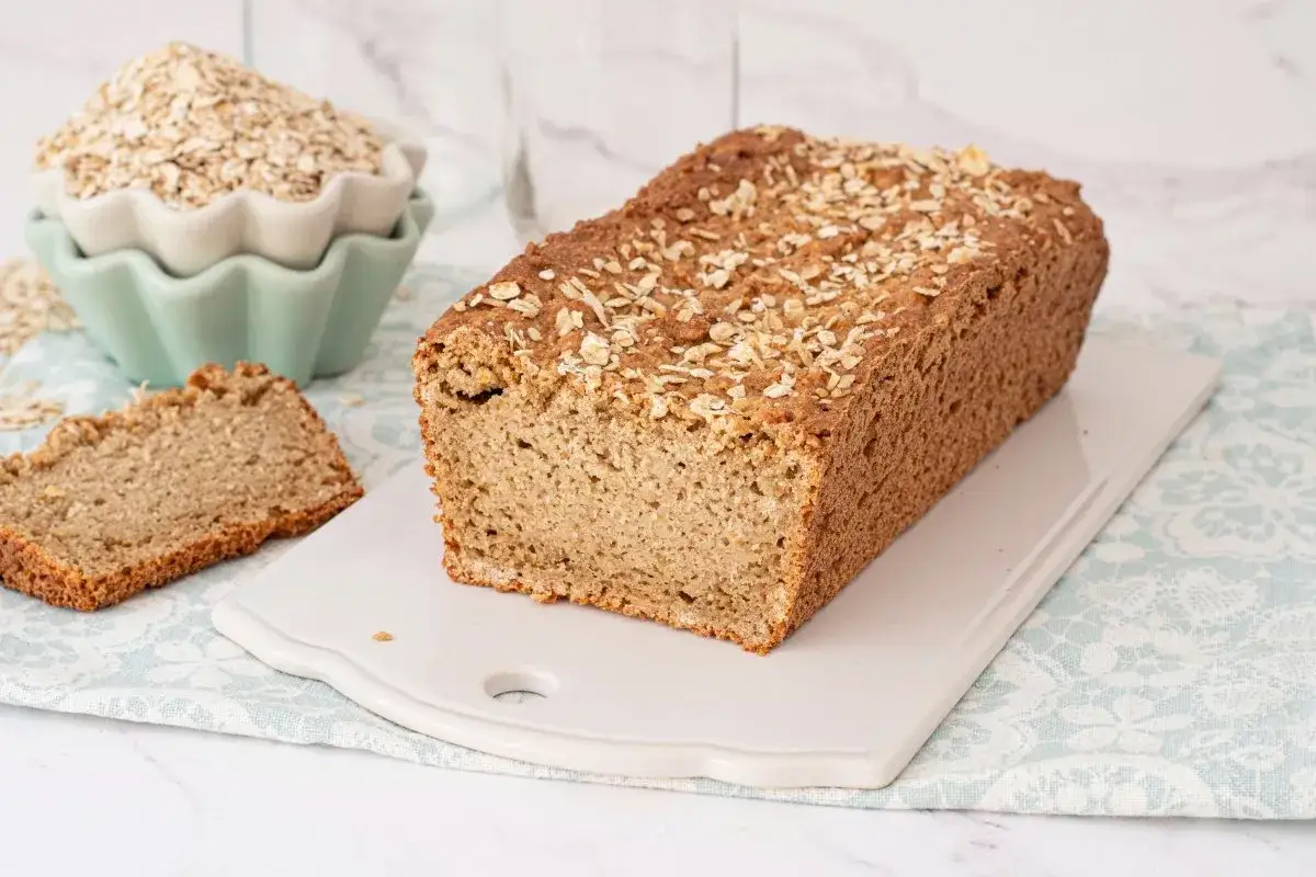 Pan integral con copos de avena, ideal para recetas con copos de avena. Un trozo cortado muestra su miga esponjosa.