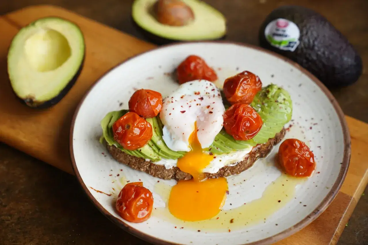 Deliciosa tosta de aguacate con huevo escalfado, tomates cherry asados y queso crema. Un desayuno perfecto.