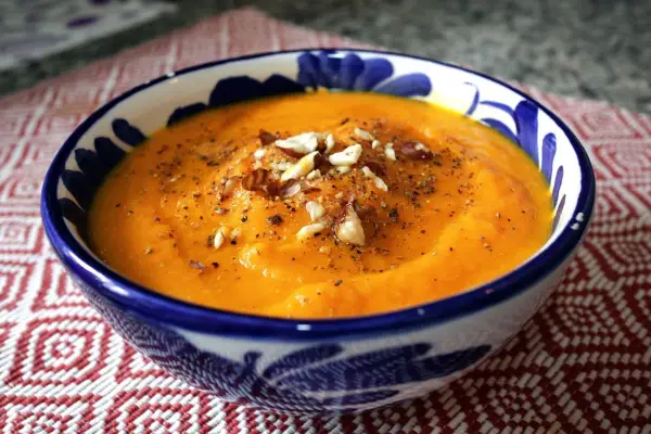 Crema de zanahoria y jengibre, servida en un cuenco azul y blanco, adornada con nueces y pimienta.