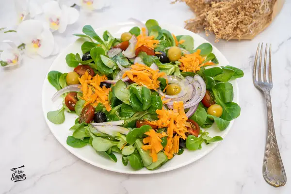 Deliciosa ensalada mediterránea con lechuga, tomate, aceitunas, cebolla morada y zanahoria rallada.