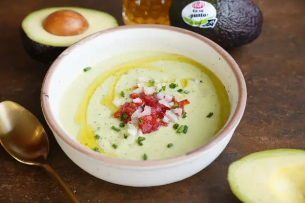 Un cremoso gazpacho de aguacate, adornado con tomate picado, cebolla y cebollino, con un chorrito de aceite de oliva.