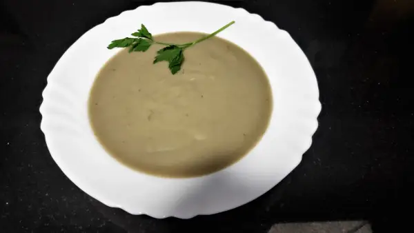 Crema de berenjena suave y sedosa, decorada con una ramita de perejil fresco, lista para disfrutar.