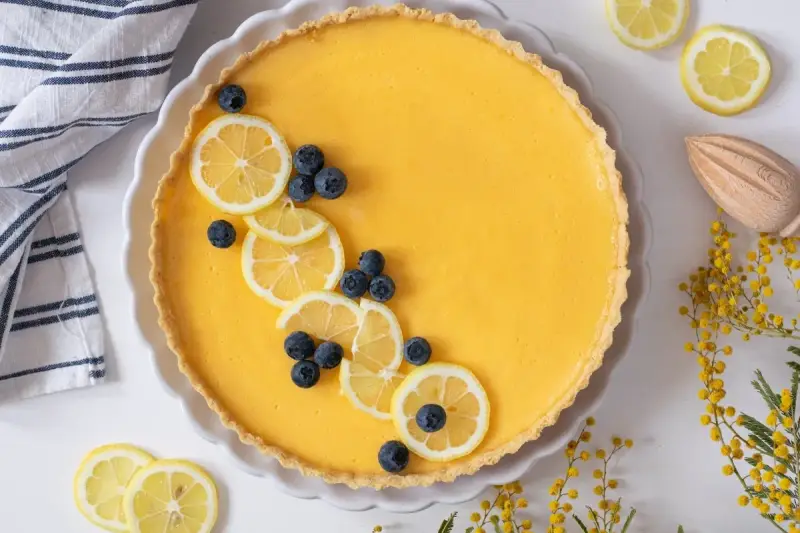Tarta de limón al horno, decorada con rodajas de limón y arándanos. Un postre refrescante y vibrante.
