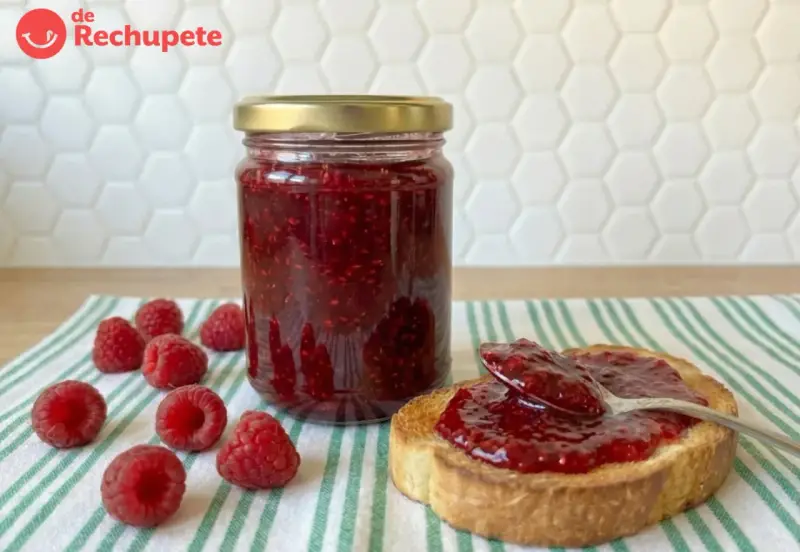 Tarro de mermelada de frambuesa casera, con frambuesas frescas y una tostada untada.