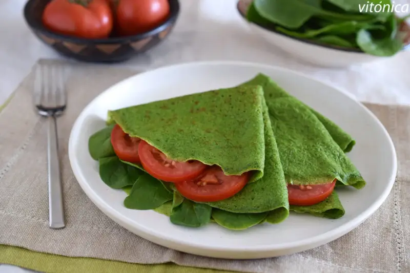 Deliciosos crepes de espinacas rellenos de rodajas de tomate fresco y hojas de espinaca, servidos en un plato blanco.