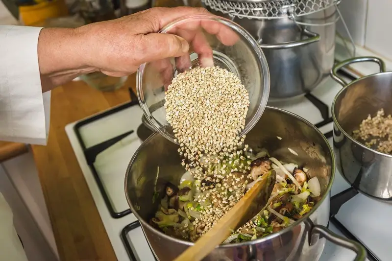 Mano añade trigo sarraceno a una olla con verduras y champiñones.