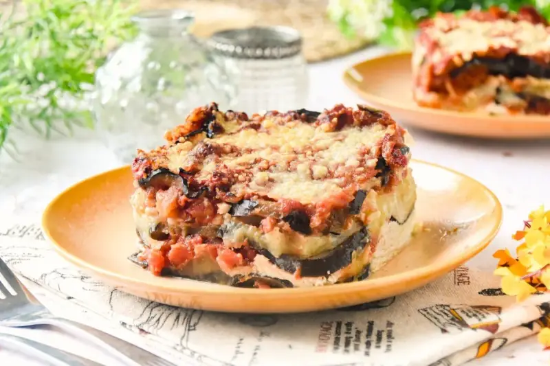 Porción de lasaña de berenjena gratinada, con capas de berenjena, salsa de tomate y queso, servida en plato naranja.